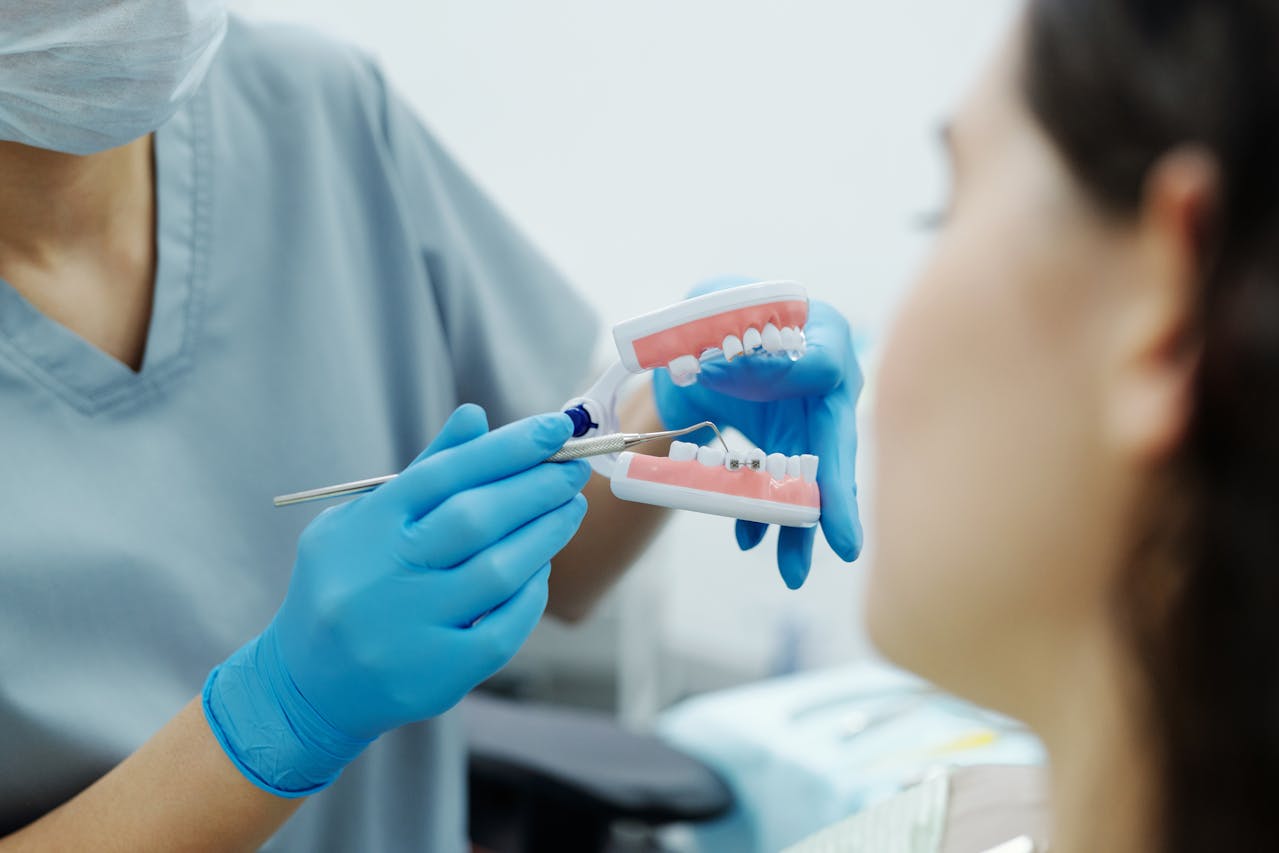A dental professional wearing blue gloves and a mask demonstrating the use of dental tools on a model of teeth