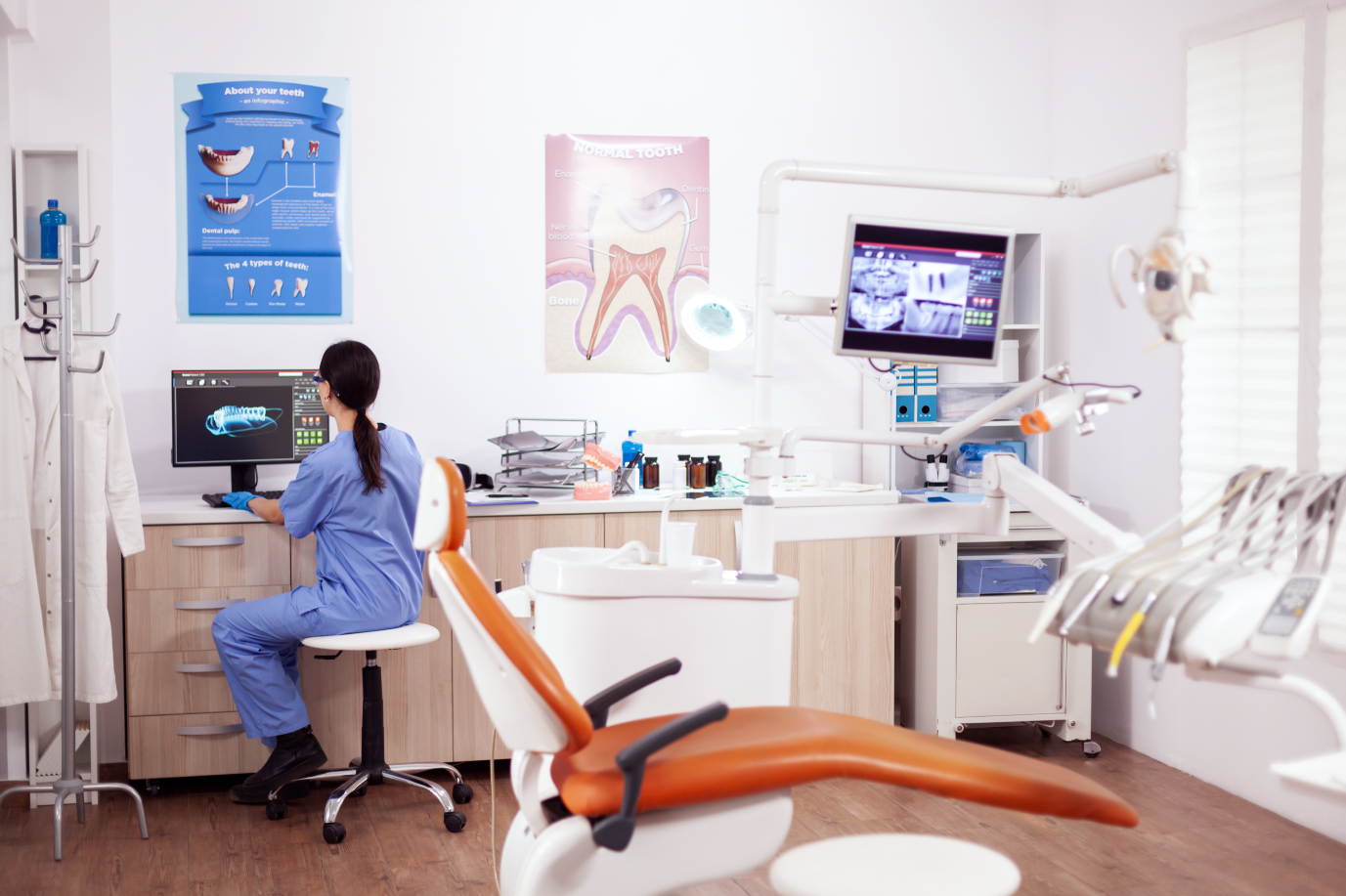 A dental professional is seated at a computer in a modern dental office, reviewing digital images of teeth