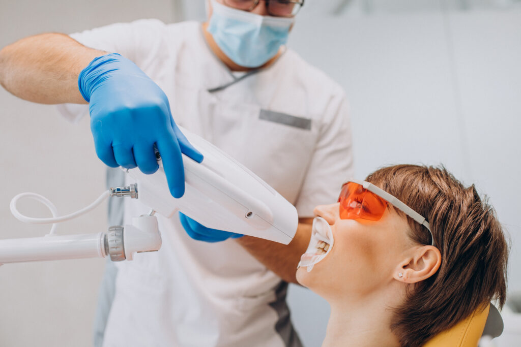 A dentist using a dental laser to whiten teeth, with the patient wearing protective orange glasses
