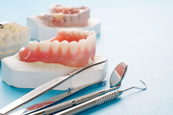 A dental setup featuring dentures, a dental mirror, and various dental tools on a blue surface