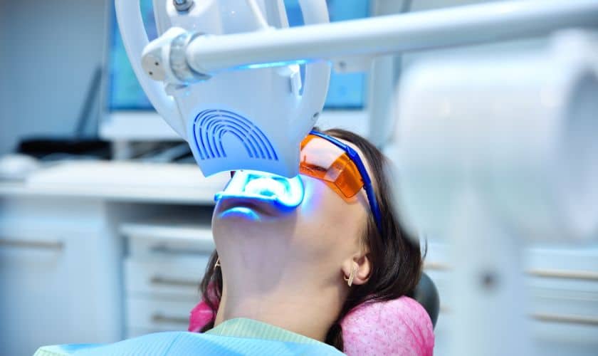 Patient undergoing professional laser or LED teeth whitening treatment at a dental clinic while wearing protective glasses.
