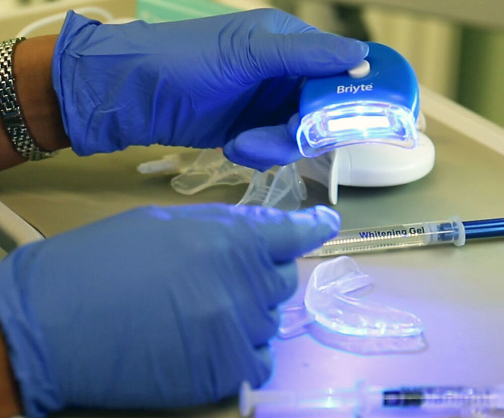 Dentist wearing blue gloves preparing a LED teeth whitening device and gel for a nano whitening procedure.