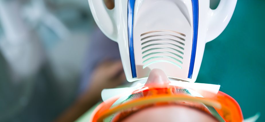 Patient undergoing professional Zoom teeth whitening treatment using a blue LED light device at a dental clinic.