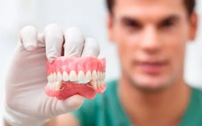 A-person-wearing-gloves-holding-a-set-of-dentures-400x250