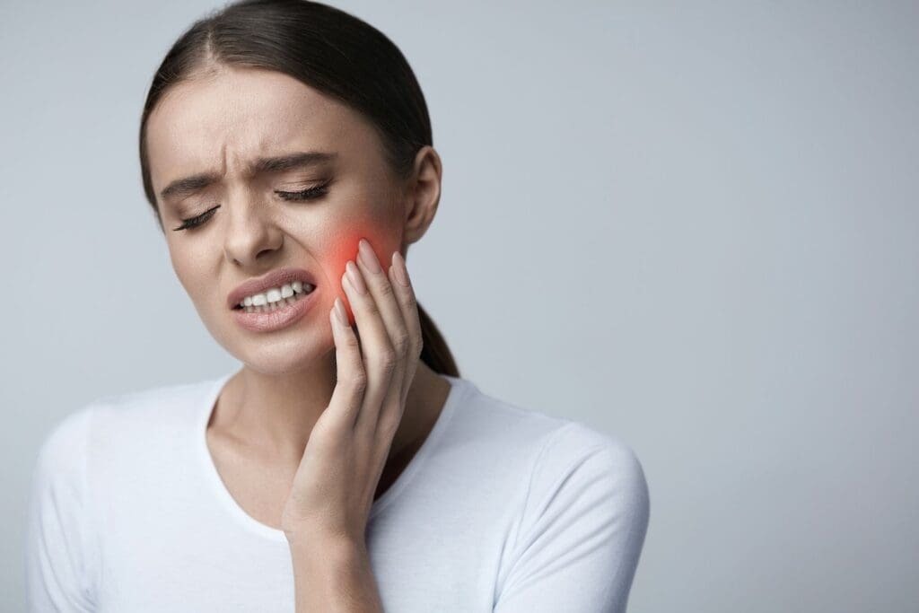 Image of a woman experiencing jaw pain with a red highlight over the TMJ area, illustrating common symptoms discussed in the article about TMJ treatment cost in Abu Dhabi.