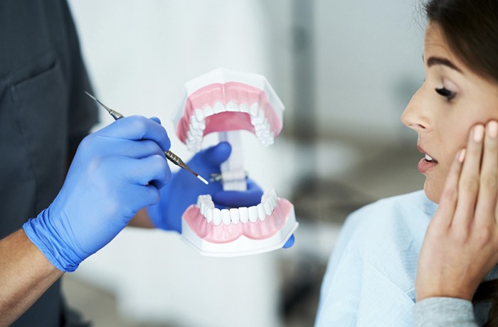 Image showing a dentist demonstrating TMJ anatomy on a dental model while a patient holds her jaw in discomfort, featured in an article about TMJ treatment cost in Abu Dhabi and available treatment options.
